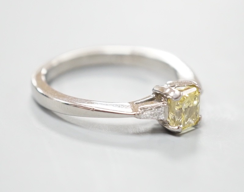 A modern platinum and single stone fancy yellow diamond set ring, with trapeze cut diamond set shoulders, size N, gross weight 4.6 grams